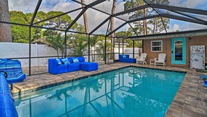 A covered outdoor swimming pool with blue cushioned seating and a view of trees and a building in the background. - St. Petersburg Escape - 3 Miles to the Beach! (St. Petersburg)