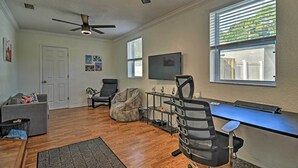 A living room with hardwood flooring, a gray sofa, a bean bag chair, a desk with a computer, and a ceiling fan. - St. Petersburg Escape - 3 Miles to the Beach! (St. Petersburg)