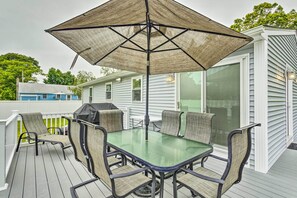 A covered outdoor patio with a glass table and chairs, a grill, and a white fence. - Narragansett Escape by Narrow River & Beaches (Narragansett)