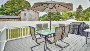 Eine Terrasse im Freien mit einem Tisch und Stühlen mit Glasplatte, einem großen Sonnenschirm und einem Grill.