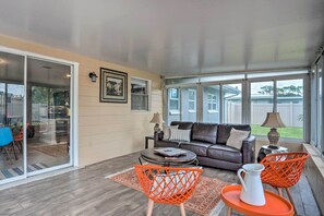 Un vaste espace de vie avec une porte-fenêtre coulissante donnant sur une terrasse, un canapé en cuir, deux fauteuils orange et une table basse.