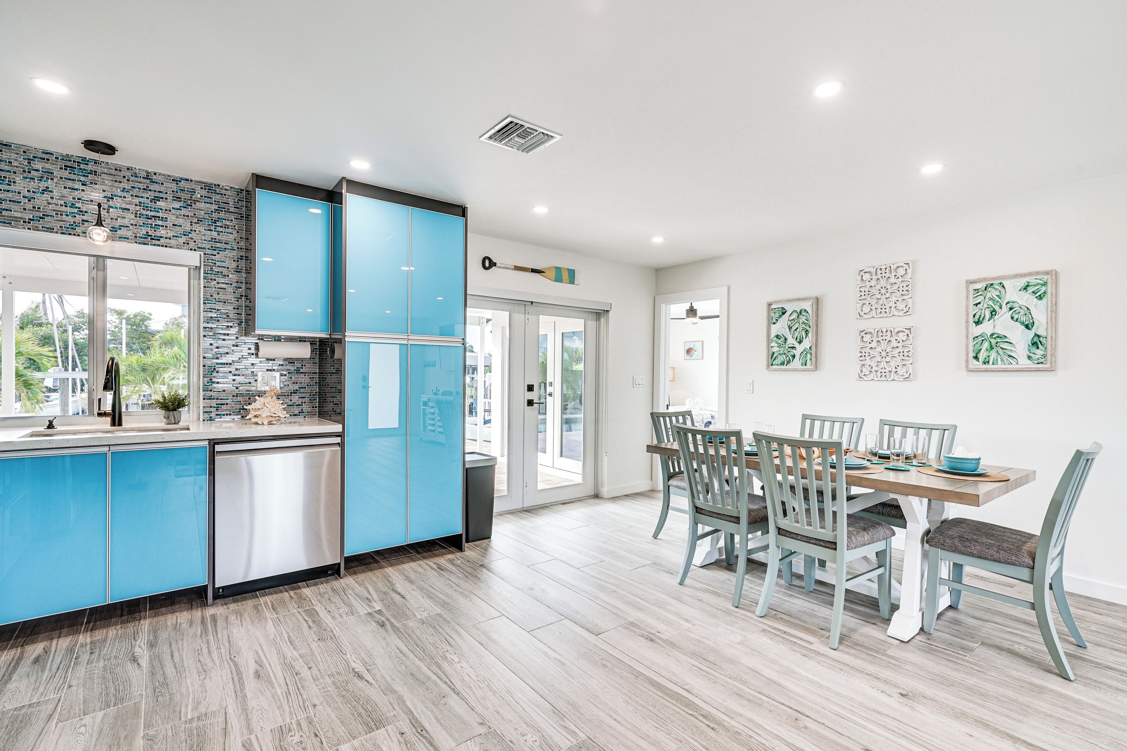 A modern kitchen with blue cabinets, a stainless steel refrigerator, and a dining area with a wooden table and chairs.