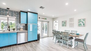 A modern kitchen with blue cabinets, a stainless steel refrigerator, and a dining area with a wooden table and chairs.