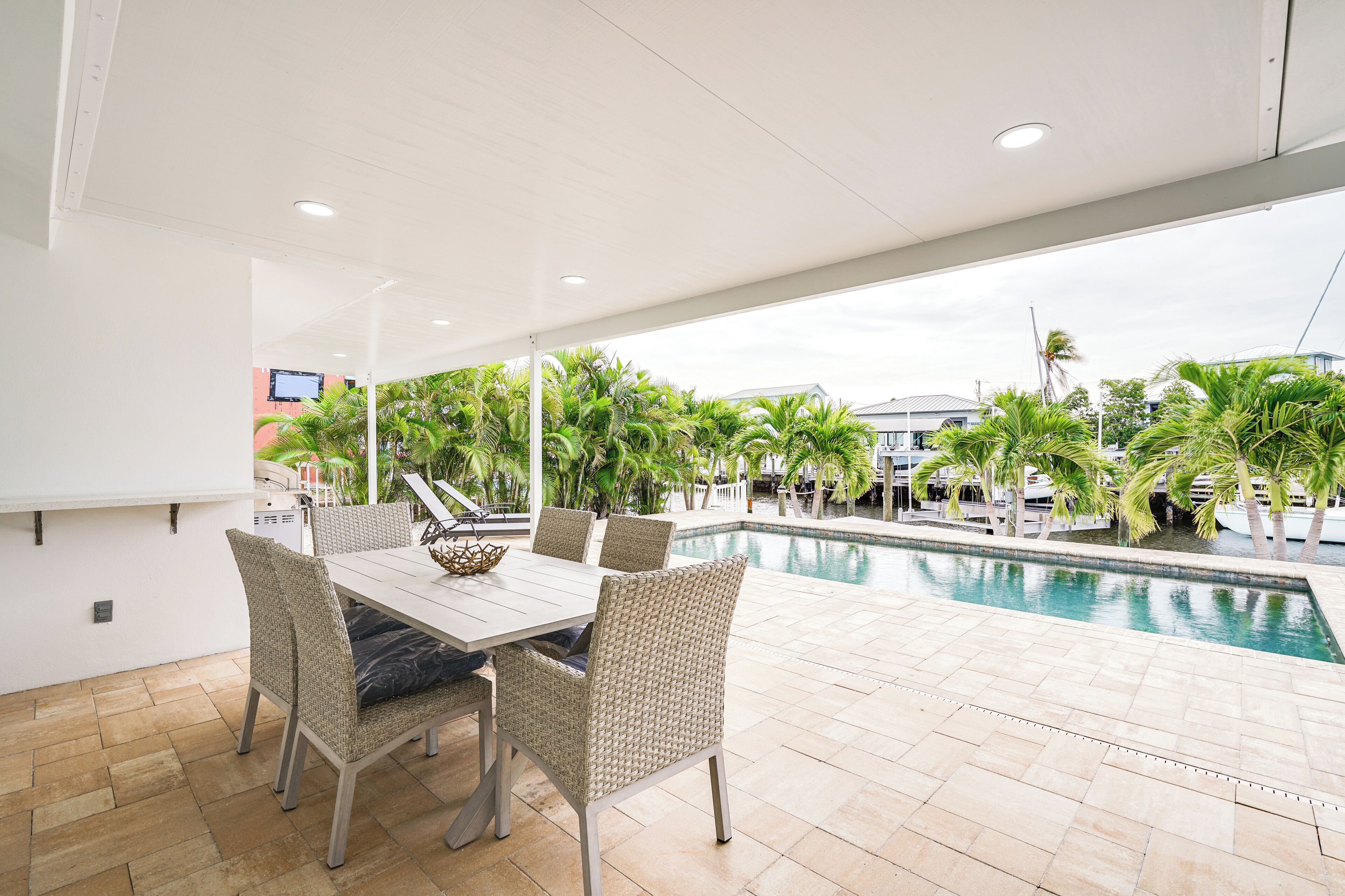An outdoor dining area with a pool view, wicker chairs, and a white table.