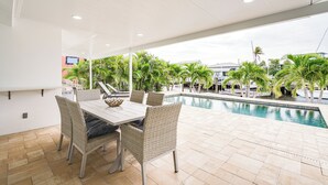An outdoor dining area with a pool view, wicker chairs, and a white table.