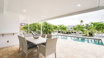 An outdoor dining area with a pool view, wicker chairs, and a white table.