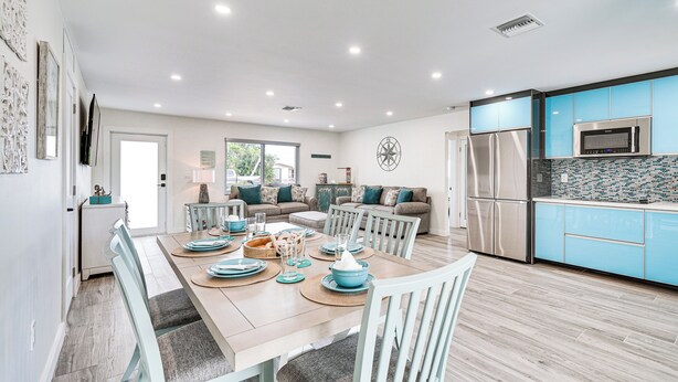 A modern kitchen with blue cabinets, stainless steel appliances, and a dining area with a wooden table set for four.