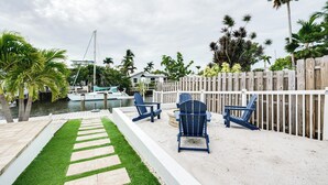 A patio area with a wooden fence, two blue Adirondack chairs, a stone pathway, and a view of a marina with boats.