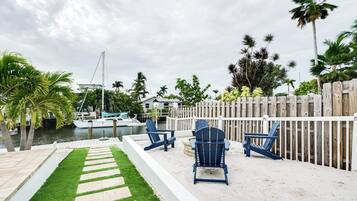 A patio area with a wooden fence, two blue Adirondack chairs, a stone pathway, and a view of a marina with boats.