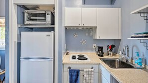 A compact kitchen with a built-in microwave, a stove, and a sink. There are starfish decorations on the wall and a towel hanging on the door. - Naples Studio w/ Resort Amenities - Near Marina! (Naples)