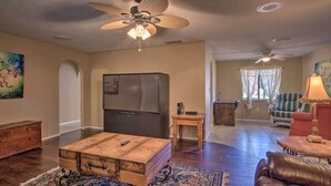 A living room with a wooden coffee table, a leather sofa, a large TV, and a ceiling fan. - Pastoral Naples Home on Working Horse Farm! (Naples)
