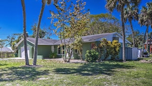 A two-story house with a green exterior, a front yard with grass and trees, and a clear blue sky. - Pastoral Naples Home on Working Horse Farm! (Naples)