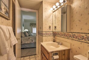 Ein Badezimmer mit einem Holzbadezimmerhocker, einem Waschbecken, einer Toilette und einem Spiegel mit Beleuchtung.