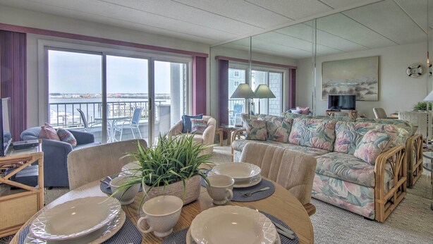 A spacious living room with large windows, a sofa, a dining table with plates and cups, and a potted plant. - 2 Mi to Ocean City Boardwalk: Gem w/ Pool + Marina (Ocean City)