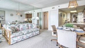 A modern living room with a floral sofa, dining table with chairs, and a kitchen area visible through an open door. - 2 Mi to Ocean City Boardwalk: Gem w/ Pool + Marina (Ocean City)