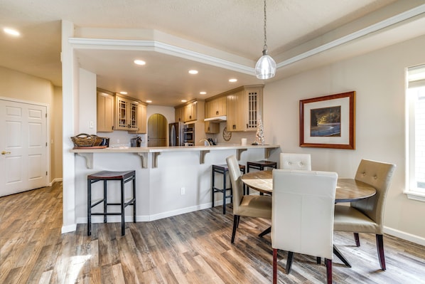 A kitchen with a central island, bar stools, and a dining table with chairs.