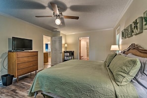 Un dormitorio con cama, ventilador de techo, televisor en una cómoda y estantería.