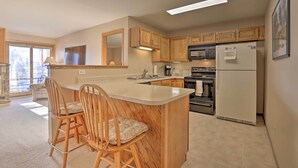 Une cuisine avec des meubles en bois, un îlot central doté de tabourets, un réfrigérateur, un four et un four à micro-ondes.