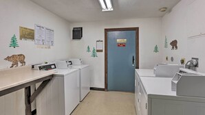 Une buanderie avec des lave-linge et des sèche-linge blancs, un panneau de commande et une porte portant l’inscription « Local des équipements d’ascenseur ».