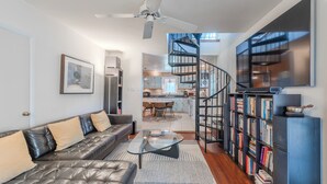 A modern living room with a leather sofa, a glass coffee table, a bookshelf, and a spiral staircase leading to a kitchen. - Dock & Bay Access! Cabin on St. Jeromes Creek (Ridge)