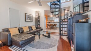 A modern living room with a leather sofa, a glass coffee table, and a spiral staircase leading to an upper level. - Dock & Bay Access! Cabin on St. Jeromes Creek (Ridge)