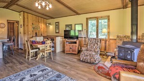 A cozy living room with a wooden ceiling, a fireplace, a television, and a dining area with a table and chairs. - Creekside Rapid City Cabin w/ Deck on 30 Acres! (Rapid City)