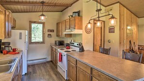 A kitchen with wooden cabinets, a stove, a refrigerator, and pendant lighting. - Creekside Rapid City Cabin w/ Deck on 30 Acres! (Rapid City)