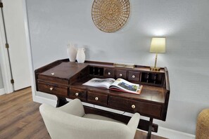 Un bureau en bois foncé, doté de nombreux tiroirs et surmonté d’une lampe, accompagné de deux vases blancs et d’une décoration murale tissée.