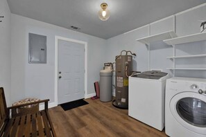 Une buanderie équipée d’un lave-linge, d’un sèche-linge, d’un chauffe-eau et d’une chaise.