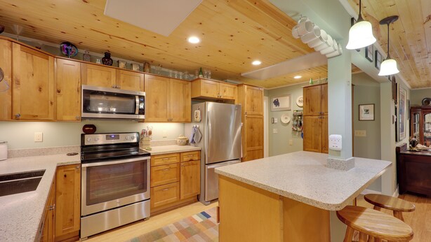 A kitchen with wooden cabinets, stainless steel appliances, a granite countertop, and a checkered rug. - Ski & Hike! Creekside Cabin 7 Mi to Linville Falls (Newland)