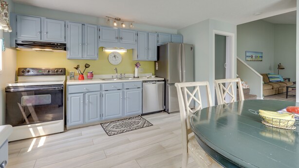 A modern kitchen with light blue cabinets, stainless steel appliances, and a dining area with a glass table. - Ideal Narragansett Location w/ Furnished Deck! (Narragansett)