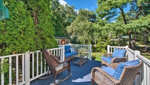 An outdoor patio with wicker furniture, a white railing, and lush greenery. - Ideal Narragansett Location w/ Furnished Deck! (Narragansett)