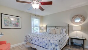 A bedroom with a bed, a ceiling fan, a bedside table with a lamp, a framed picture on the wall, and a window with curtains. - Ideal Narragansett Location w/ Furnished Deck! (Narragansett)