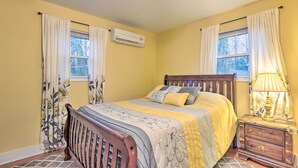 Une chambre à coucher avec un lit en bois, deux fenêtres avec des rideaux, un climatiseur et une table de chevet avec une lampe.