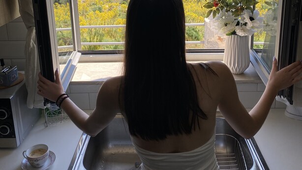Una cocina con un ventanal, un lavamanos y un florero con flores en el alféizar.