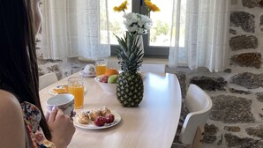 Un comedor con pared de piedra, una mesa dispuesta con frutas, una piña y un mantel estampado con motivos florales.