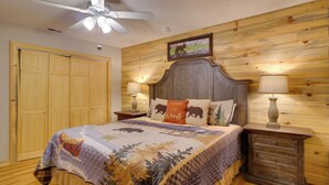 Quarto com cabeceira de madeira, colcha com estampas de floresta e animais, duas luminárias de cabeceira e um ventilador de teto.