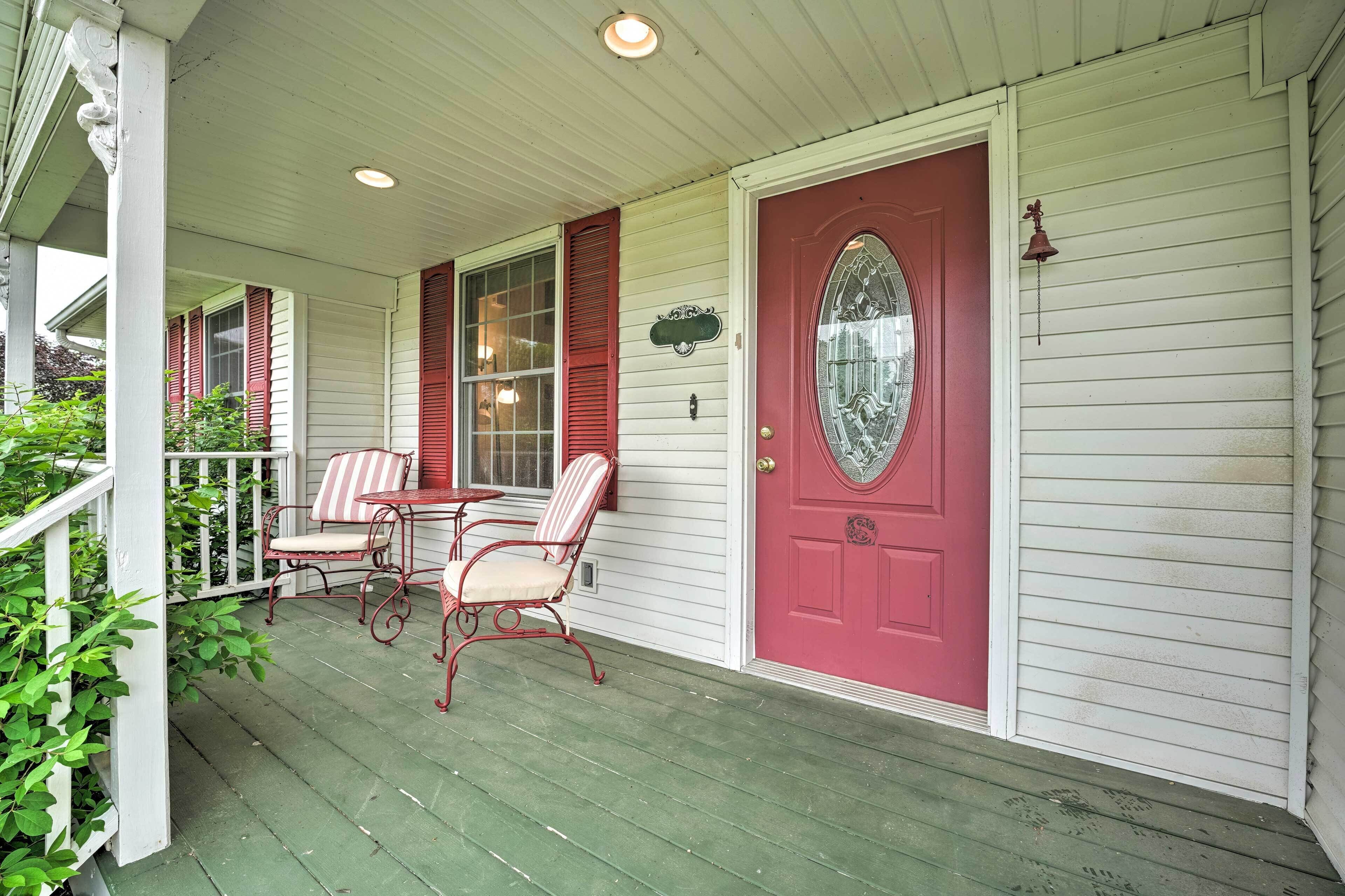 A porch with a red door, white shutters, and a small table with chairs.