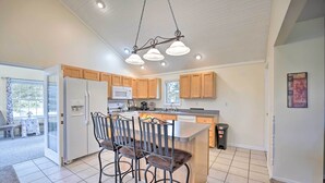 Une cuisine moderne avec des meubles en bois, un îlot central doté de tabourets, un réfrigérateur, un four à micro-ondes et un évier.
