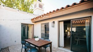 A patio with a wooden table and chairs, a brick floor, and a sliding glass door leading to an interior space. - Scottsdale Condo w/ Patio, Pool & Hot Tub! (Scottsdale)