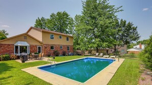 A rectangular swimming pool with a concrete deck, surrounded by a well-maintained lawn and a brick house with a red roof. - Family-friendly West Chester Twp Home w/ Pool! (West Chester)