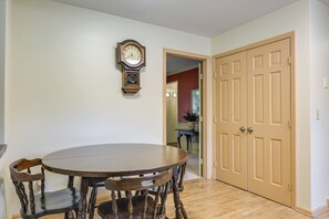 A dining area with a round wooden table and chairs, a wall-mounted clock, and a closed door. - Family-friendly West Chester Twp Home w/ Pool! (West Chester)