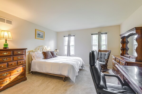 A bedroom with a bed, dresser, chair, and a large mirror. - Family-friendly West Chester Twp Home w/ Pool! (West Chester)