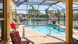 A covered pool area with a view of a body of water, a chair, and a potted plant. - Cape Coral House w/ Private Dock, Pool & Bar! (Cape Coral)