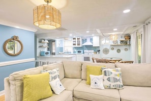 A modern living room with a beige sofa, yellow and white patterned cushions, a round mirror, and a wicker pendant light. - Walk to Ocean: Home w/ Fire Pit in Atlantic Beach (North Myrtle Beach)