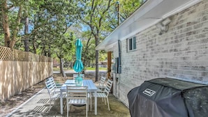 A patio with a table and chairs, a covered grill, and a white building with a brick exterior.