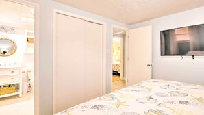 A bedroom with a bed, a TV mounted on the wall, and a bathroom with a mirror and sink.