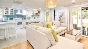 A modern kitchen with white cabinets, a dining area with a beige sofa, and a large window with a view of the outdoors.