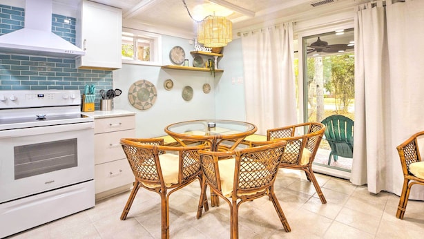 A kitchen with white appliances, a round glass table, wicker chairs, and decorative plates on the wall.