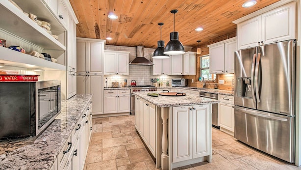 Una cocina amplia con armarios blancos, una isla central, electrodomésticos de acero inoxidable y techo de madera.